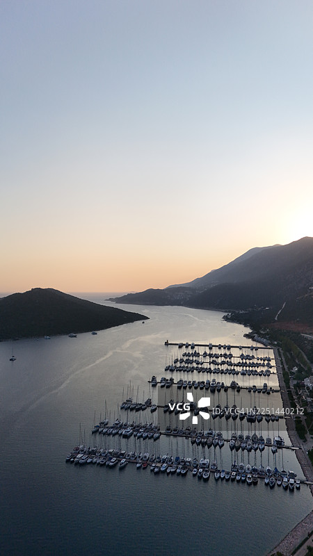 高角度俯瞰宁静的码头，夕阳下停泊着许多船只，码头依偎在群山与平静的海之间图片素材