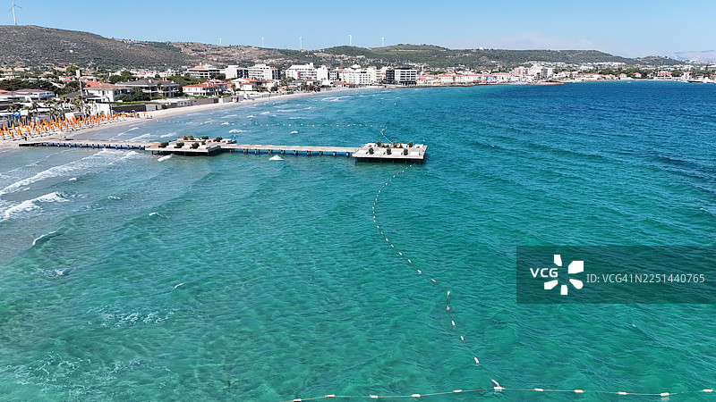 碧海蓝天下的海岸小镇，远山风力发电机与海滨沙滩，码头尽收眼底图片素材