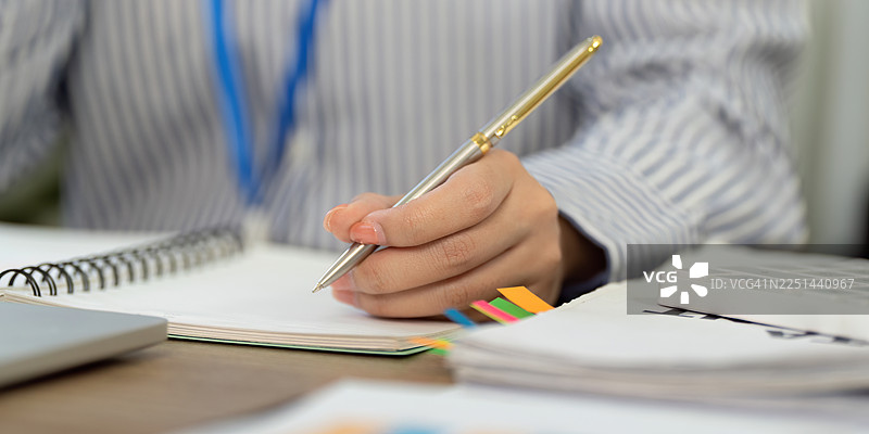 职业女性在办公桌前写笔记的特写，展现专业环境中的专注与高效图片素材