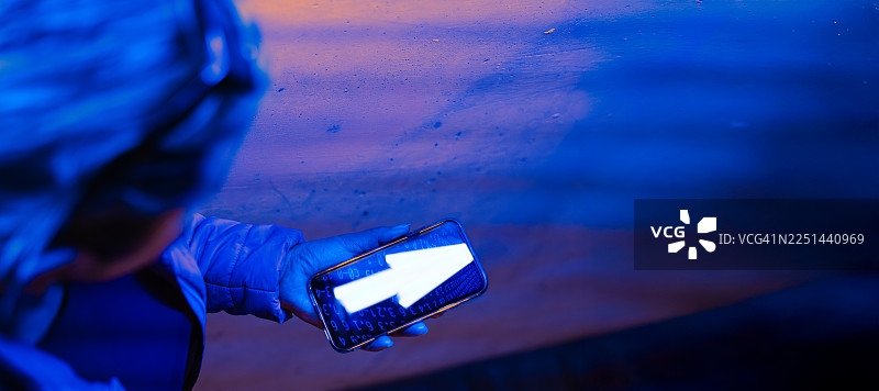 在黑暗的蓝光环境中，特写一个人拿着一部带有发光箭头图标的手机，指示导航或进度图片素材