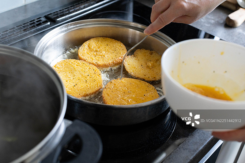 特写一只手在炉灶上的平底锅里准备法式吐司，旁边有一个装有蛋液的碗图片素材