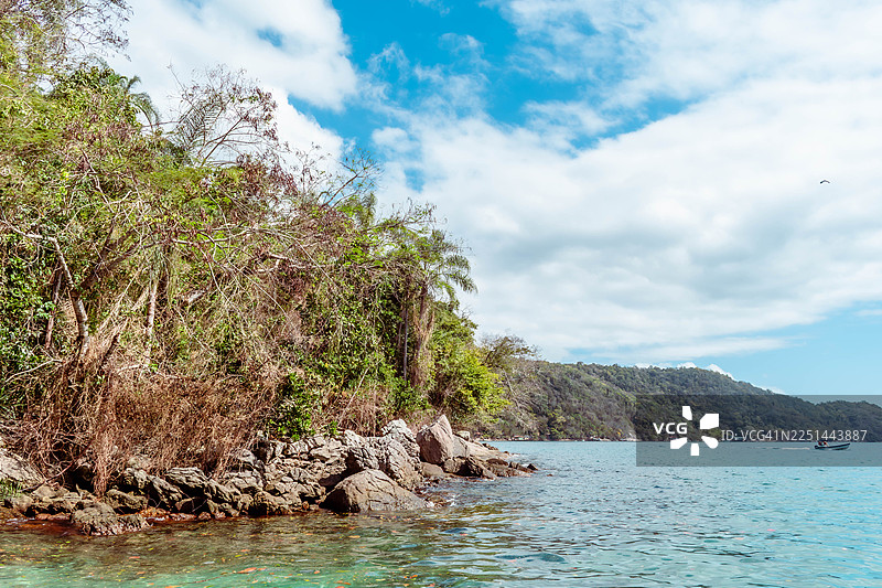 郁郁葱葱的绿色热带海岸，拥有清澈碧绿的海水、一艘小船，天空湛蓝，点缀着云彩。图片素材