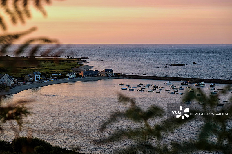法国夕阳下宁静的海湾，有如画般的海岸村庄和船只，四周环绕着葱郁的植被。图片素材