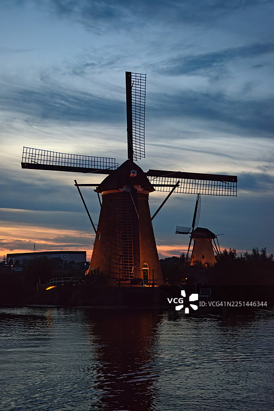 夕阳下的荷兰传统风车在宁静的运河上形成剪影，地点：金德代克，荷兰图片素材