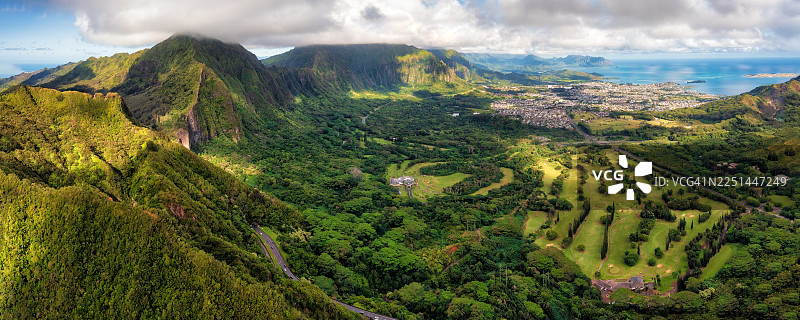 云层密布的天空下，郁郁葱葱的山谷、高尔夫球场和海滨城市组成的壮丽全景航拍图图片素材