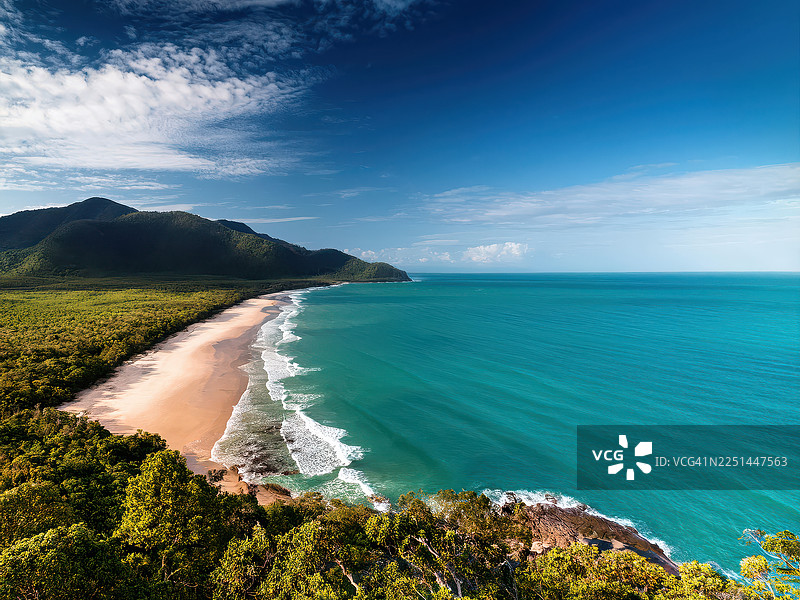 澳大利亚道格拉斯角特里布尔逊，郁郁葱葱的绿山与碧绿的海洋在晴朗的蓝天下交汇，令人惊叹的原始热带海滩鸟瞰图图片素材