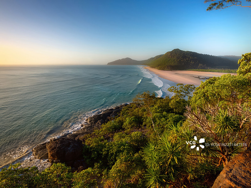 澳大利亚道格拉斯角海角在日出时分的壮丽海岸景色，郁郁葱葱的绿山与原始的沙滩和碧绿的海水相接图片素材