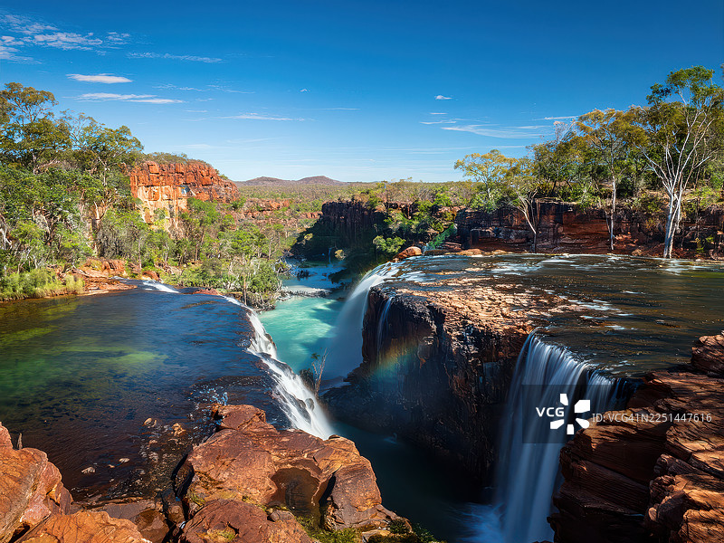 雄伟的瀑布从古老的红岩上倾泻而下，天空湛蓝，周围绿树成荫，构成一幅令人惊叹的自然风光，澳大利亚，金伯利图片素材