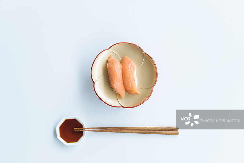 白色背景上，上方直视镜头的三文鱼寿司，配有酱油和筷子图片素材