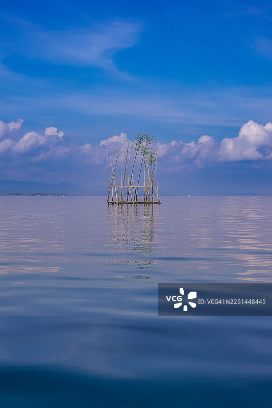 宁静的蓝天和平静的水面，载着一艘小竹筏，倒映着宁静的景象，孟加拉国吉大港图片素材