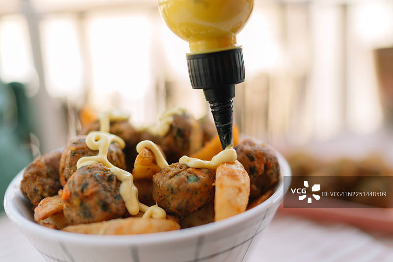 碗里放着装有脆炸土豆和肉丸的碗，上面淋着芥末酱，碗放在桌子上图片素材