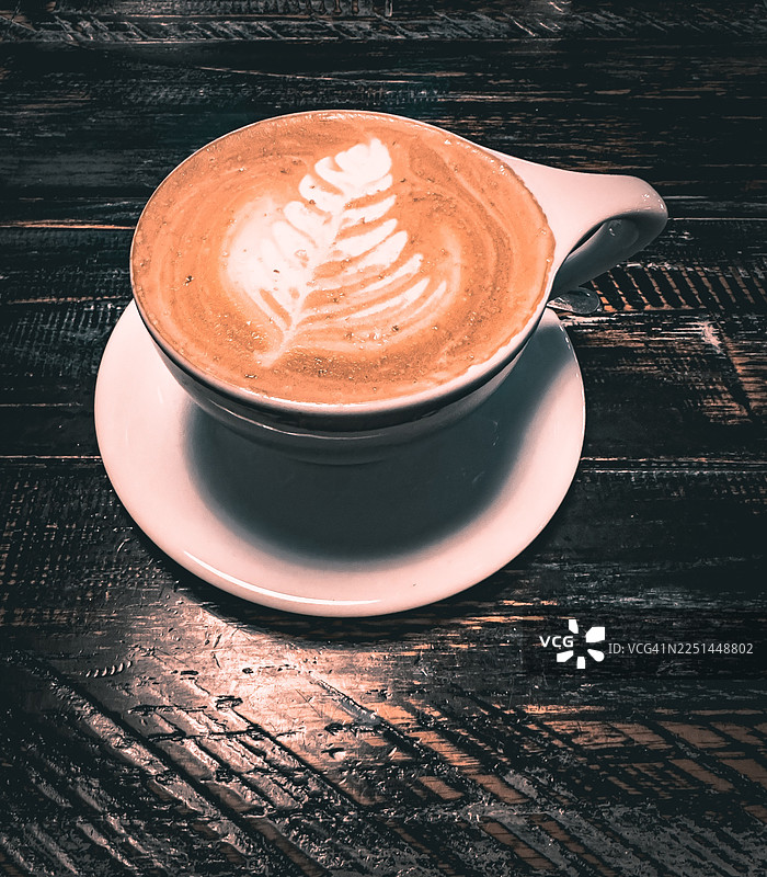 俯视角度拍摄的美味卡布奇诺，上面有拿铁艺术，放在质朴的木桌上，非常适合悠闲的咖啡时光图片素材