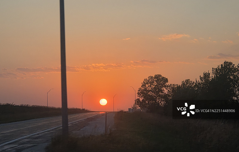 美国韦伯斯特县，乡村公路上色彩鲜艳的日落，树木和电线杆剪影图片素材