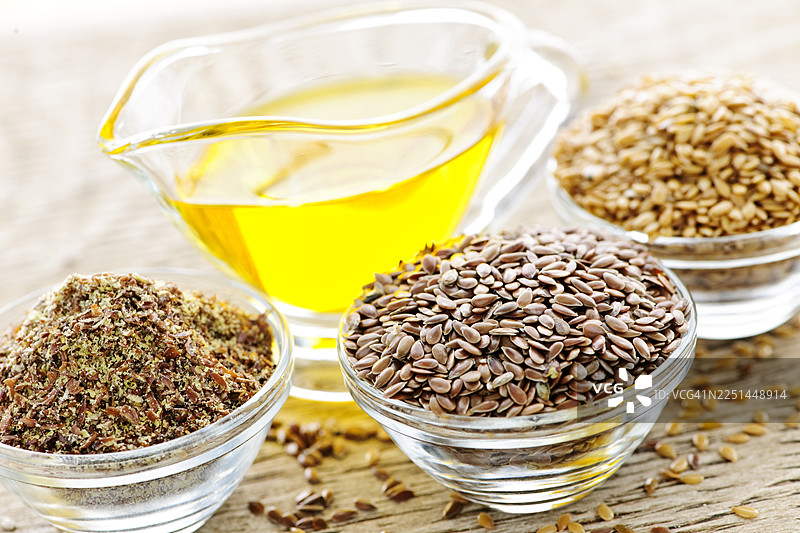 特写镜头：木桌上的碗里装着亚麻籽油、整颗亚麻籽和磨碎的亚麻籽，强调健康饮食图片素材