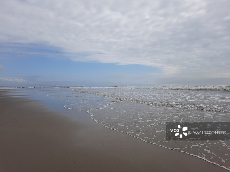 宁静的海滨风光，多云的天空下，温柔的海浪轻拍着沙滩，提供一处宁静的自然避世之所图片素材