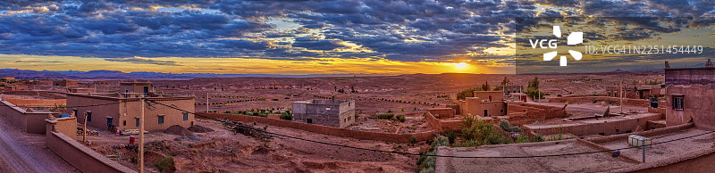 摩洛哥斯库拉日落时分的广阔沙漠景观，点缀着零星建筑和戏剧性的云彩图片素材