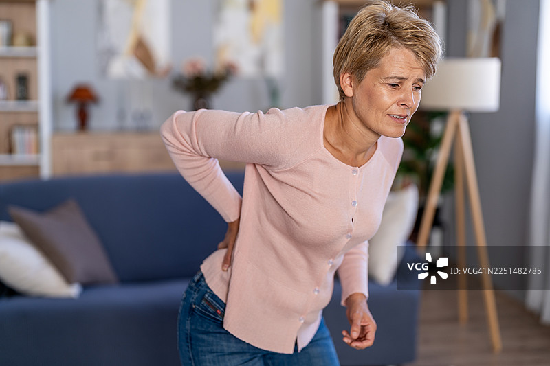 一位成熟的女性在家中感到下背部疼痛图片素材