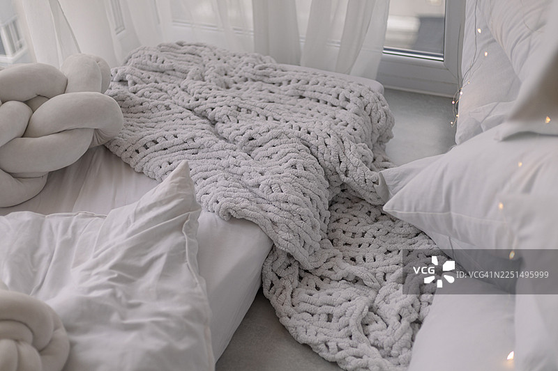 节日卧室里，柔软的床铺铺设着洁净的白床单和轻盈的粗针织毯。图片素材