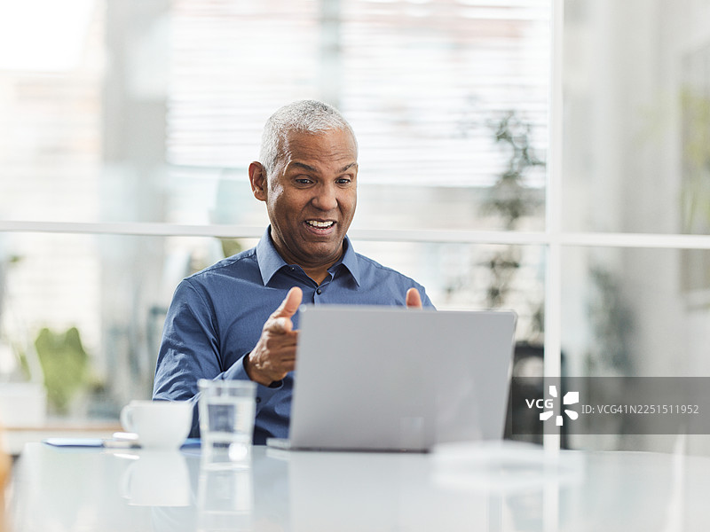 一位快乐的西班牙裔老年商人在办公室进行视频通话。图片素材