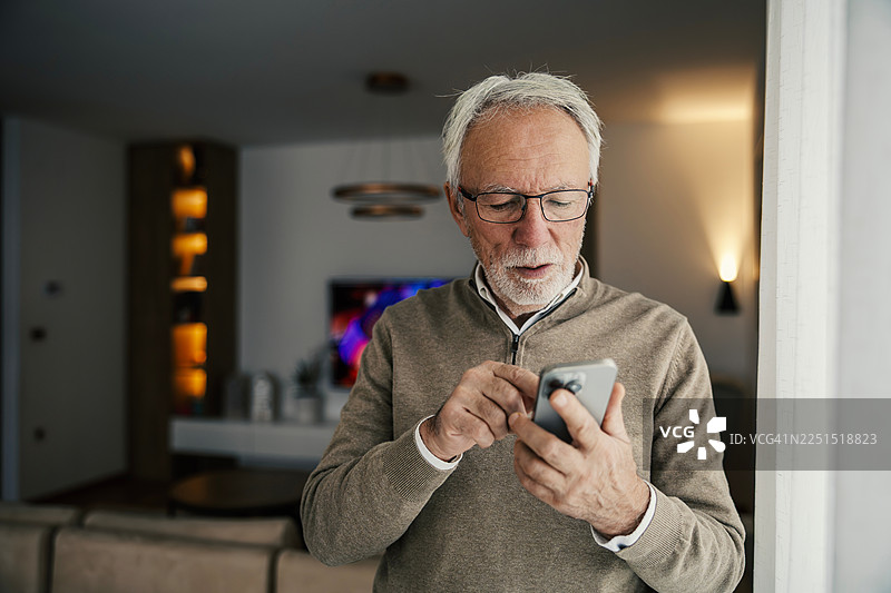 一位年长男子在家中使用智能手机，与科技连接图片素材