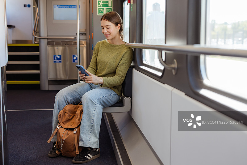 年轻女子坐在火车上，使用手机图片素材