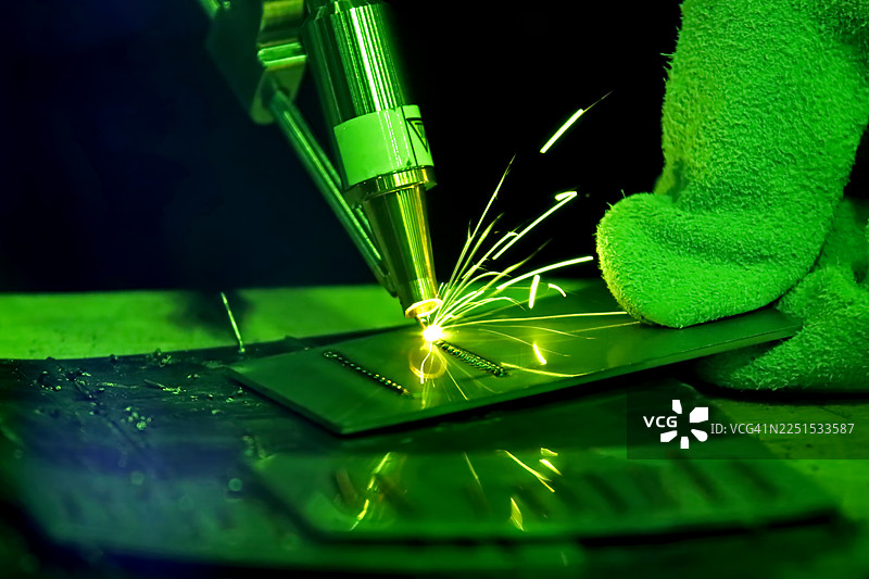 特写镜头：工业激光头在金属表面进行精密焊接或切割，工人的安全绿色手套正在监督高科技制造过程图片素材