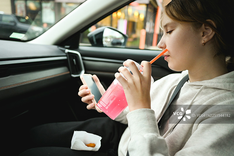 青少年在车内一心多用，一边喝东西一边玩手机图片素材
