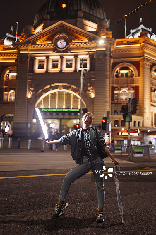 夜间城市街道上，一名女子手持光剑摆姿势图片素材