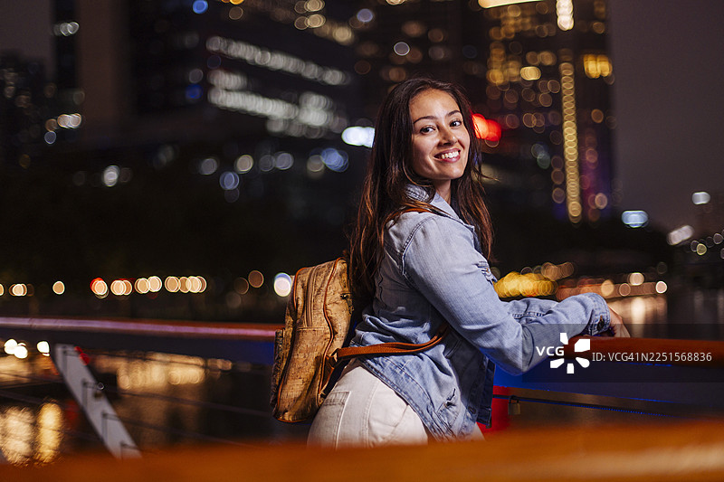 微笑着的女士在栏杆旁享受夜间城市漫步图片素材