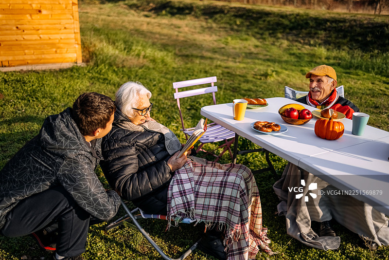 老人们在山脚下的 cottages 房前共度时光，一起阅读图片素材