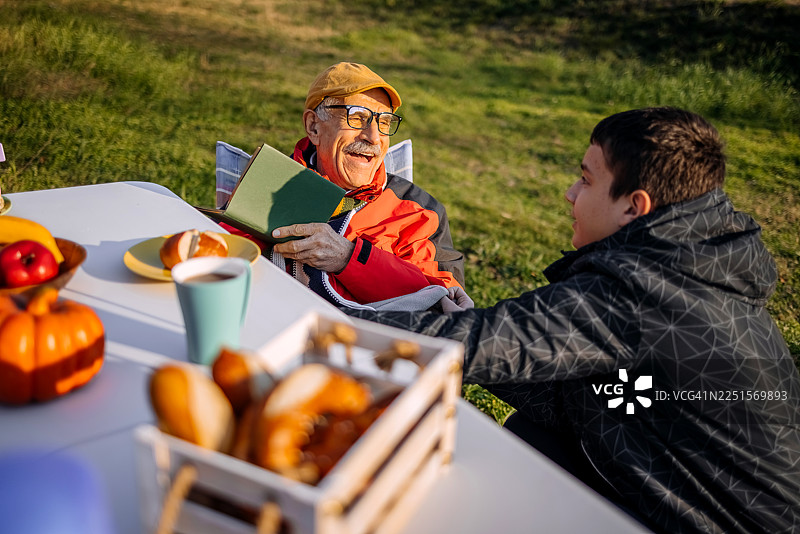 老人们在山脚下的农舍前聚在一起，在户外读书。图片素材