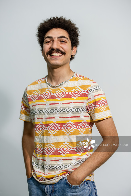 年轻的中东男子穿着色彩鲜艳的T恤，面带微笑，背景为白色图片素材