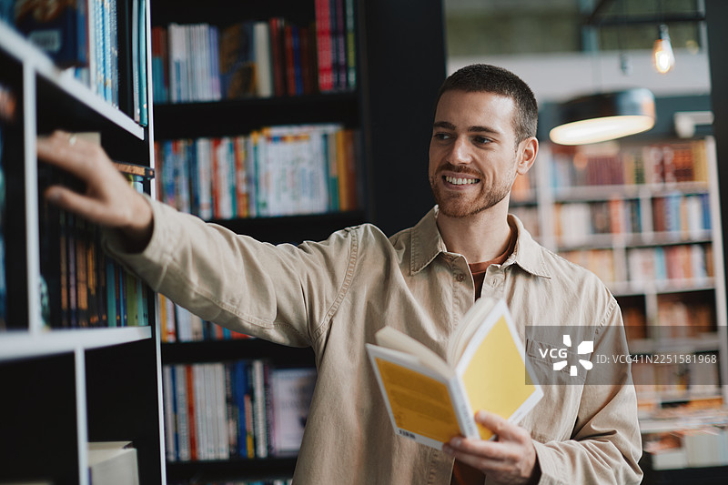 一位快乐的成年男子在舒适的图书馆里阅读一本黄色的书，面带微笑，享受休闲时光图片素材