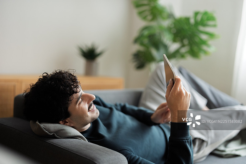 男人在家中放松地躺在沙发上，使用平板电脑图片素材
