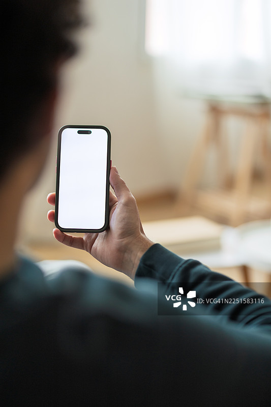 一个人在家中，手持一部屏幕空白的智能手机图片素材