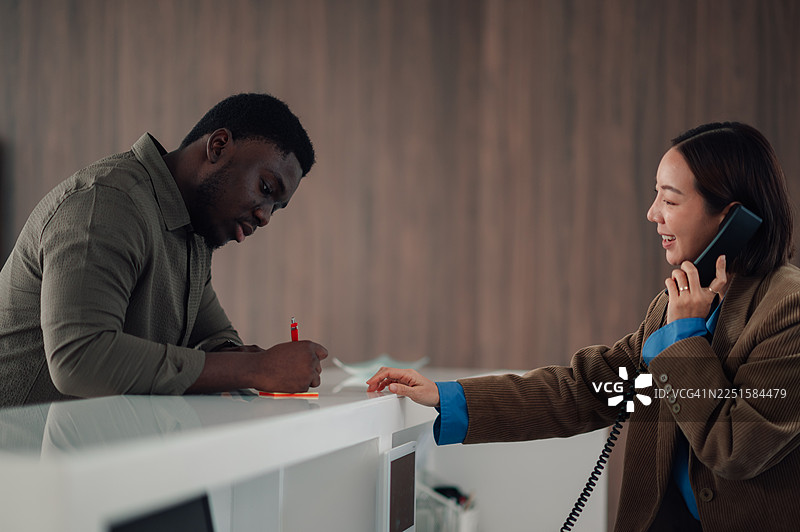 一名男子在接待处填写表格，一名女子正在打电话图片素材