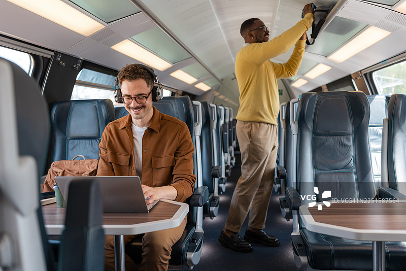 一名年轻男子正在使用笔记本电脑，另一名乘客正准备坐下图片素材