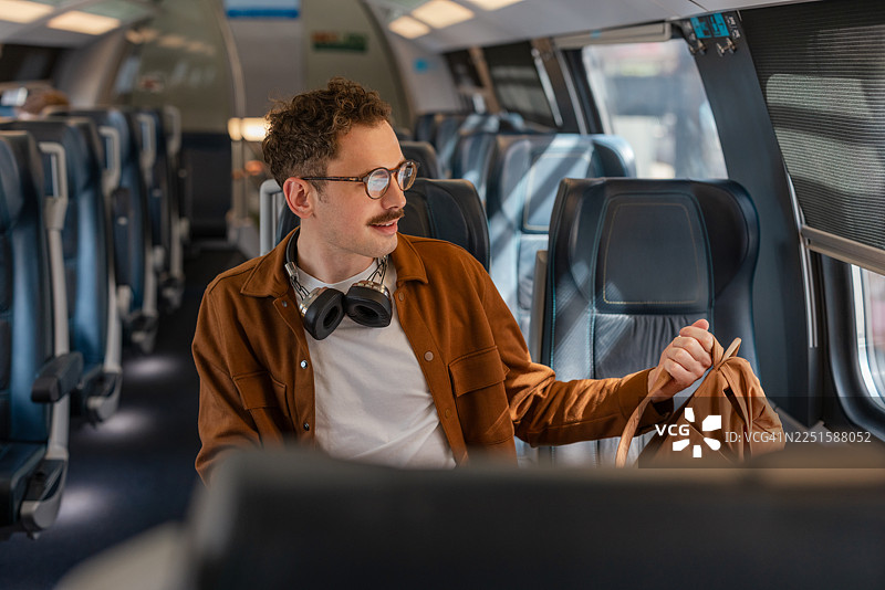 戴眼镜、戴耳机、独自一人乘坐现代火车旅行的年轻男子图片素材