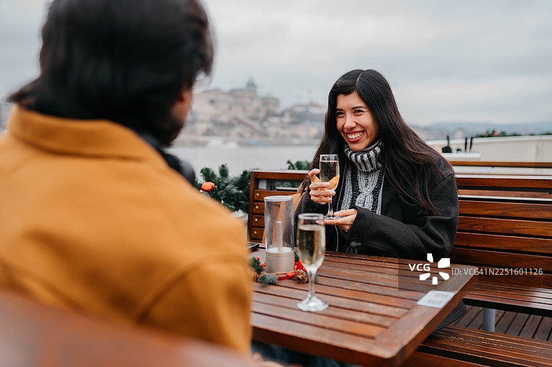 一对情侣在阴天的下午，在城市区域的户外餐桌旁享用饮品，背景是城市景观。图片素材
