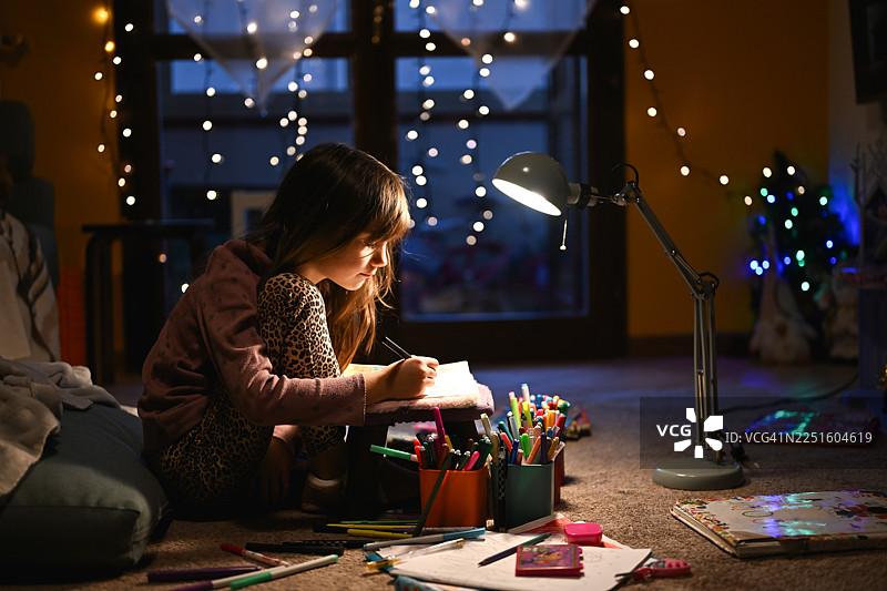 小女孩在地板上画画，享受温馨的夜晚图片素材