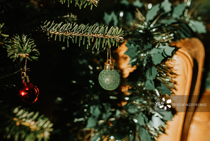 一个闪闪发光的绿色圣诞装饰球挂在圣诞树上，旁边是闪光彩带和冬青装饰。图片素材