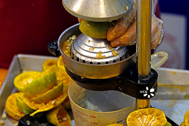 戴着塑料手套的手在手动榨汁器中挤压橙子的特写图片素材