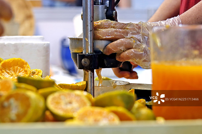 制作夏日饮品。机械榨汁机榨取水果的特写，背景是废弃的橙子皮图片素材
