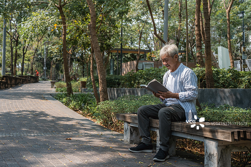 一位年长的男士在公园里宁静地阅读书籍图片素材