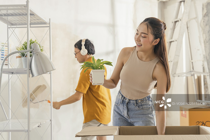 恩爱亚洲情侣快乐地站着，在新公寓里，在房屋翻新和室内装饰项目中布置家具，象征着快乐的乔迁和改善。图片素材