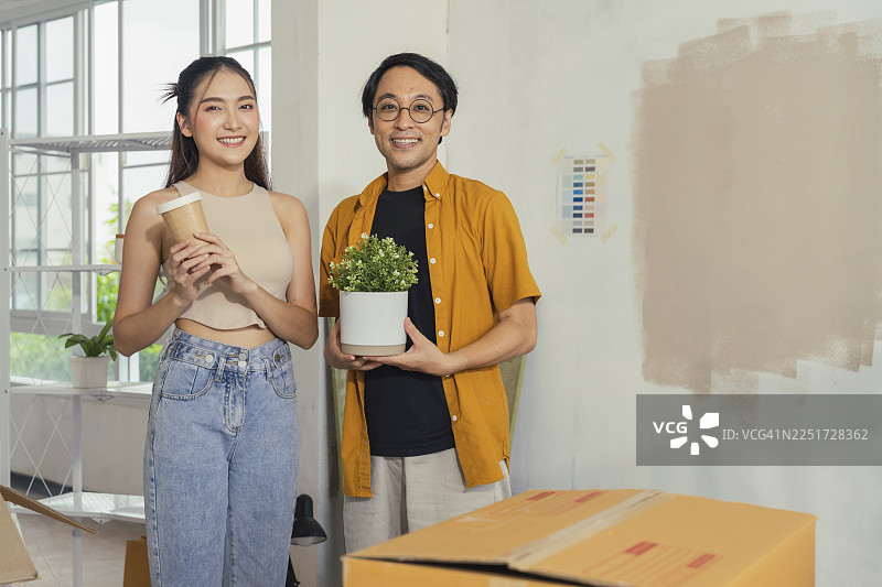 一对年轻的亚洲情侣穿着休闲服，在新公寓里整理和拆箱组装家具，忙于DIY翻新和搬家，开心地展示着箱子，憧憬着未来的家。图片素材