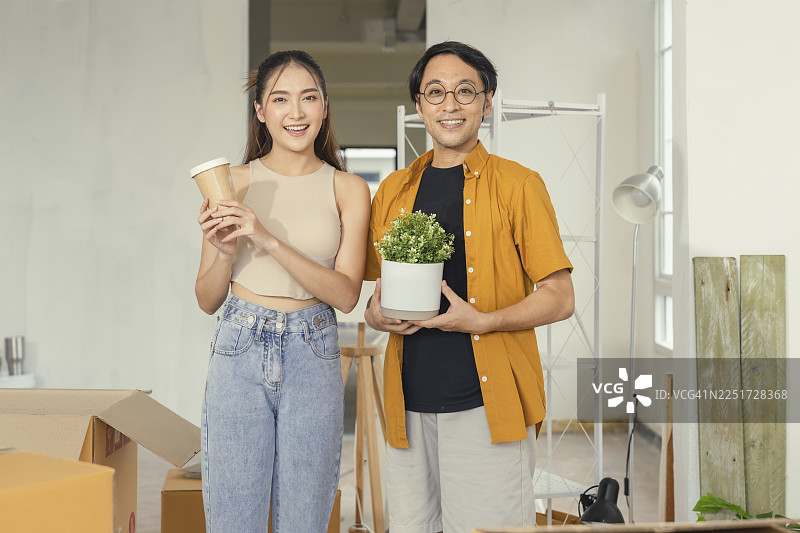 恩爱的一对亚洲情侣幸福地站在新公寓里，在房屋翻新和室内装饰项目中布置家具，象征着愉快的搬家和改善生活。图片素材