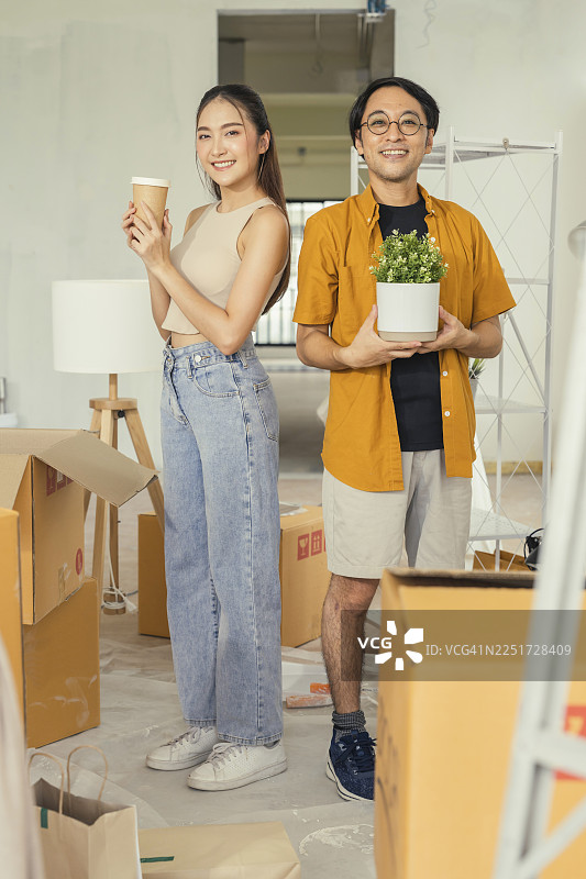 一对年轻的亚洲情侣穿着休闲服，在新公寓里整理和拆箱组装家具，进行DIY翻新和搬家，开心地展示着箱子并憧憬着未来的家。图片素材