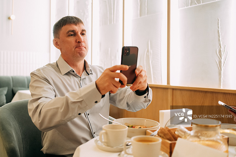 男人在餐厅用智能手机拍摄食物图片素材