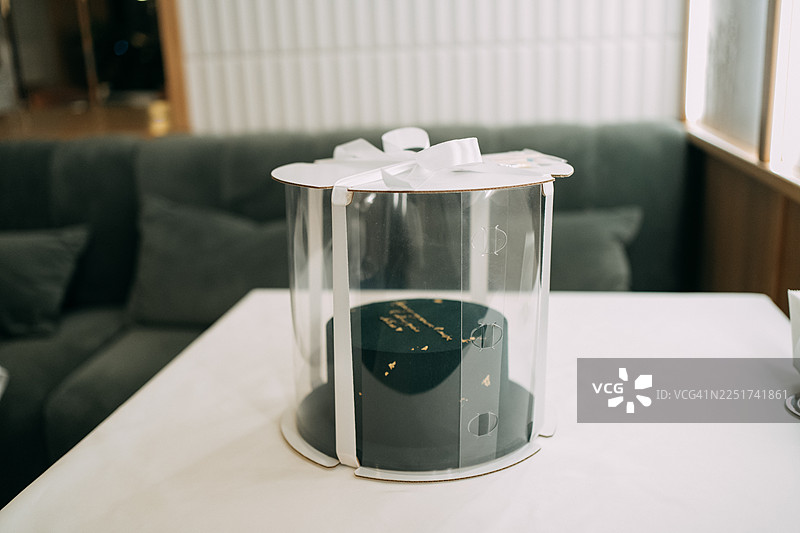 礼品包装盒里的深色蛋糕，上面有金色的题字，摆放在桌子上。图片素材